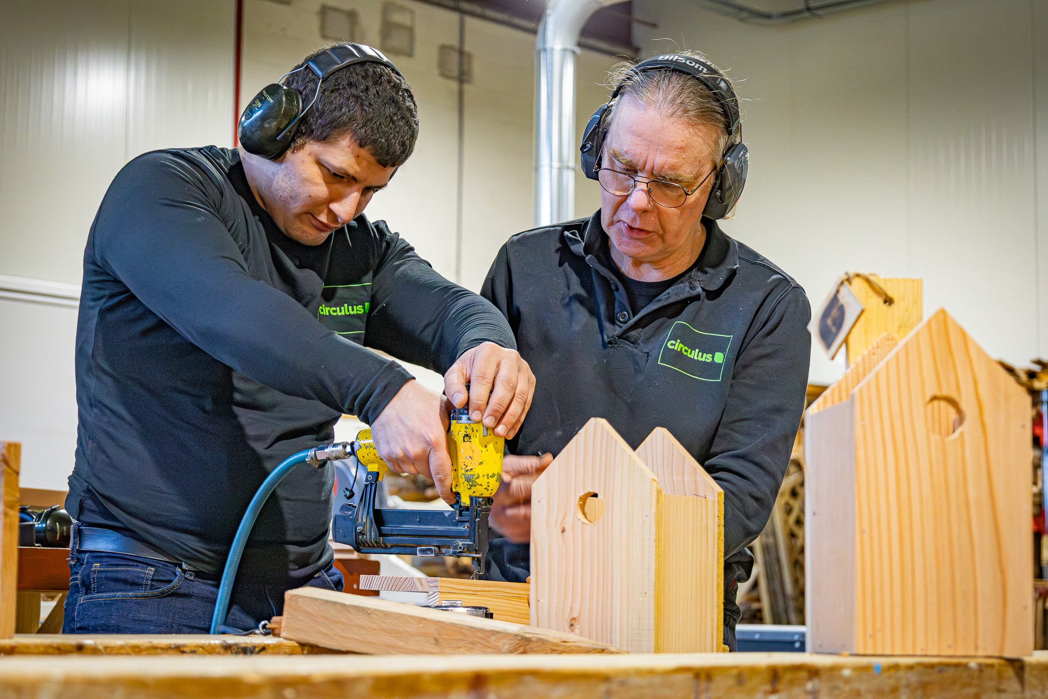 Medewerker krijgt begeleiding tijdens houtbewerking in een werkplaats.